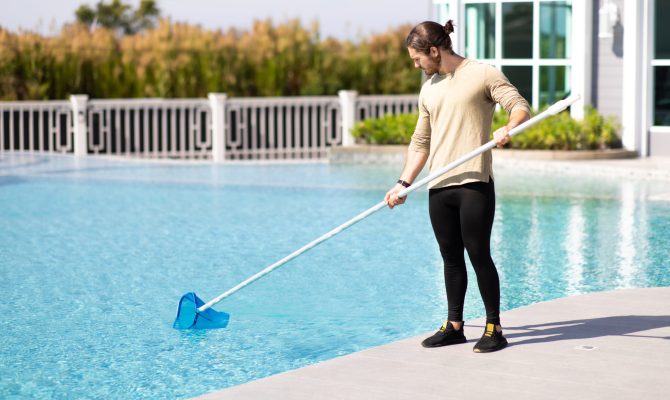 Young man professional cleaner worker cleaning pool with scoop net outdoors.